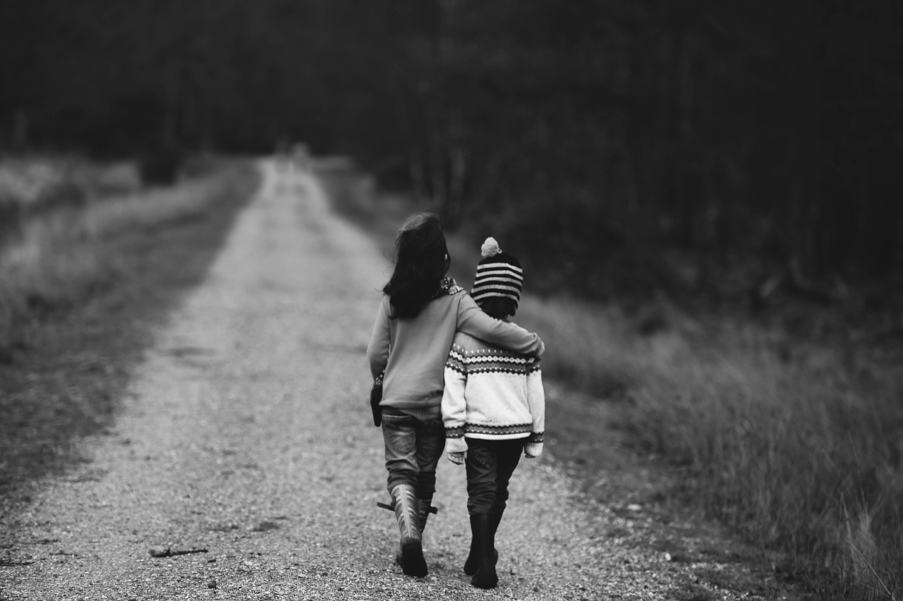 Protecting the next generation. A young black brother and sister walking down a dirt path. The girls arm is around the shoulder's of her brother.